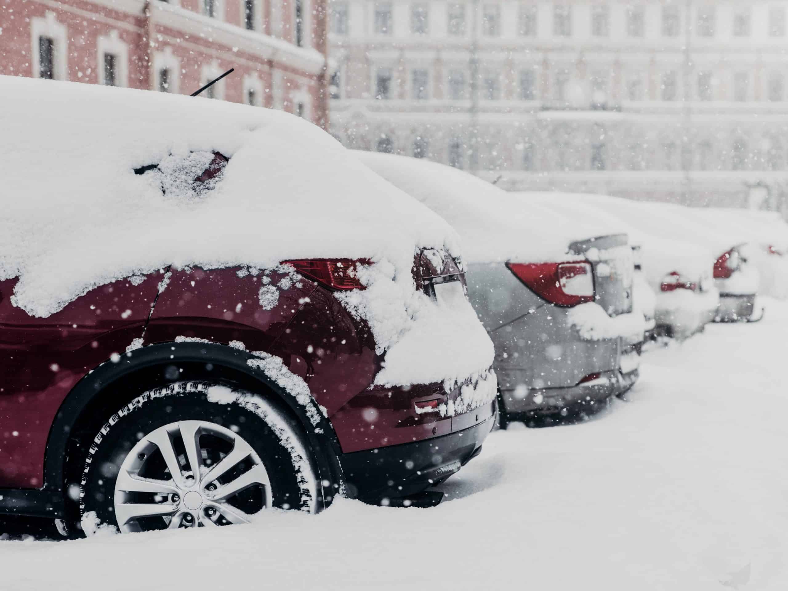 Parked cars stuck in snow after heavy snowstorm stand at parking lot. January snowfall in city. Transportation and vehicles covered with white thick layer of snow